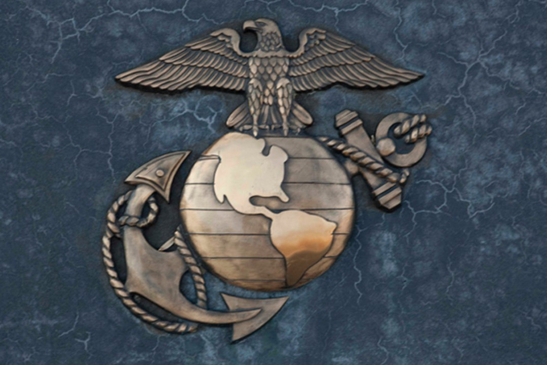 Metallic Marine Corps emblem (eagle, globe, and anchor) on a blue, textured background.