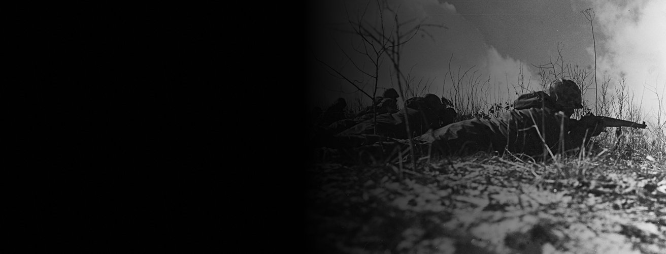 A black and white image of Marines fighting during the battle of Chosin Reservoir. They are on their stomachs, aiming their rifles.