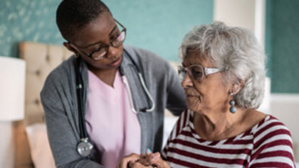 A female health aide standing next to an older woman in her home. 