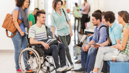 A group of students talking in a hallway, one is using a wheelchair.