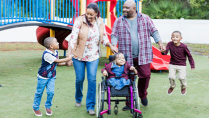 Two parents playing at a playground with their young children, one is using a wheelchair.