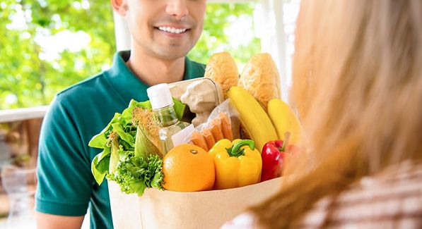 Smiling delivery man giving grocery bag to woman customer at home for online food shopping service concept