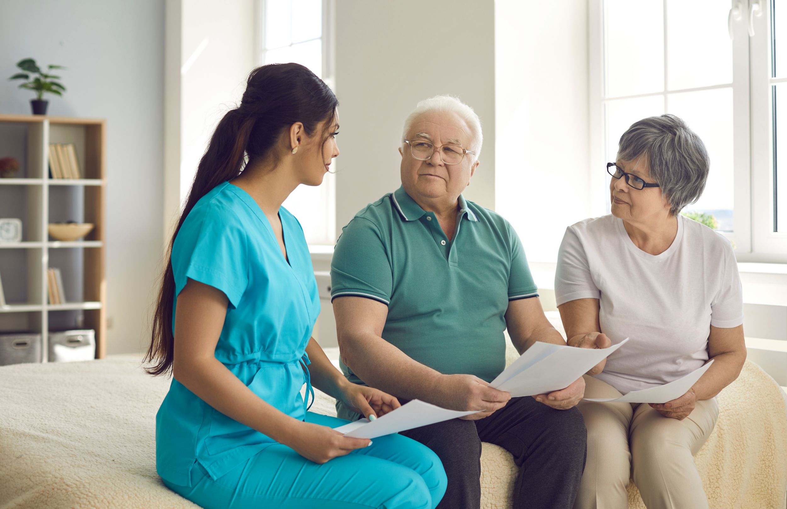Caretaker helps senior patients sign homecare agreement, fill informed exam consent, understand test result or health insurance details. Grandparents discuss professional home care nurse service costs