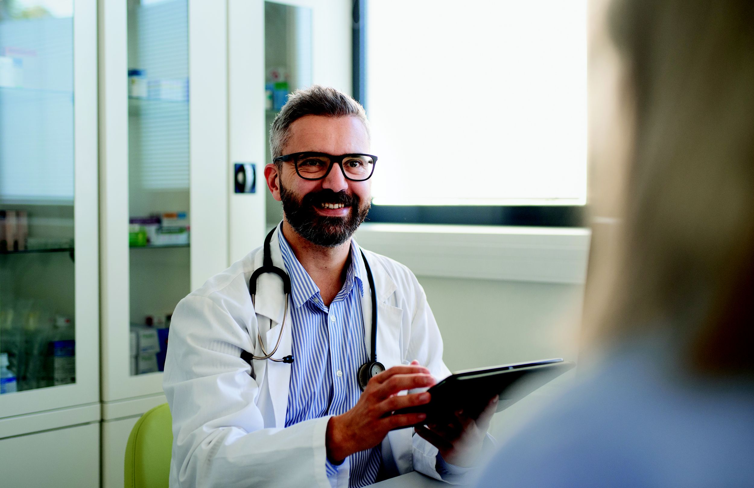 Cheerful doctor talking with his patient in doctors office at hospital.
