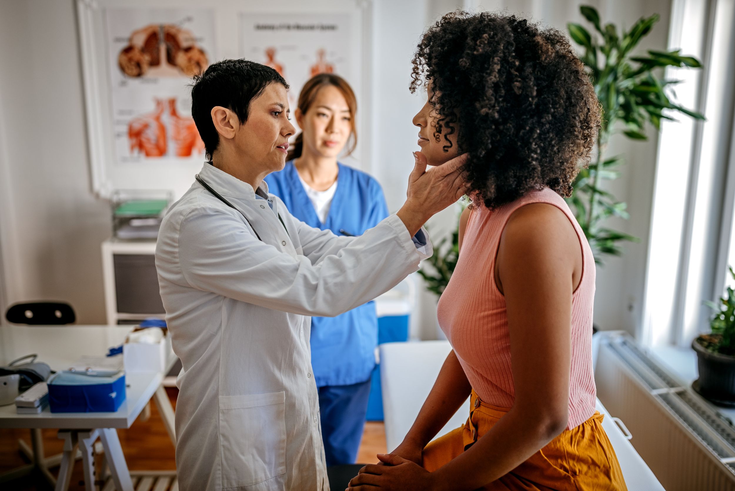 Female doctor examining a female patient in his medical office while female nurse writing information about patient