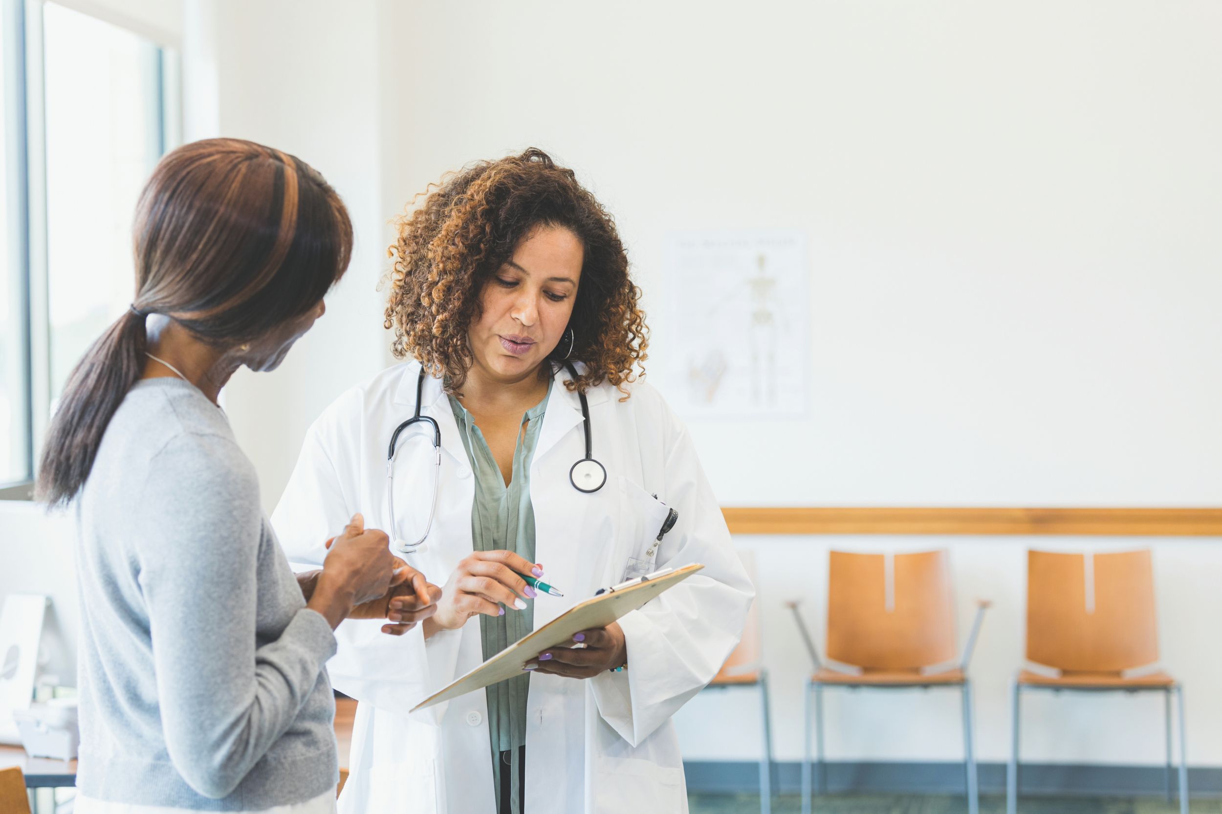 A mid adult female doctor explains a female patient's test results. The doctor points at something on the results that are on a clipboard.