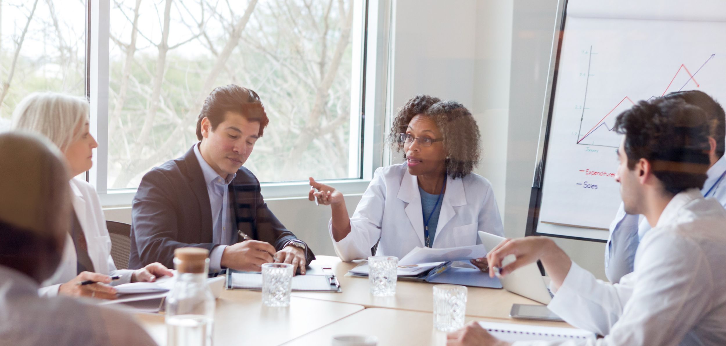 Mature female doctor gestures while discussing something during a healthcare conference with colleagues.