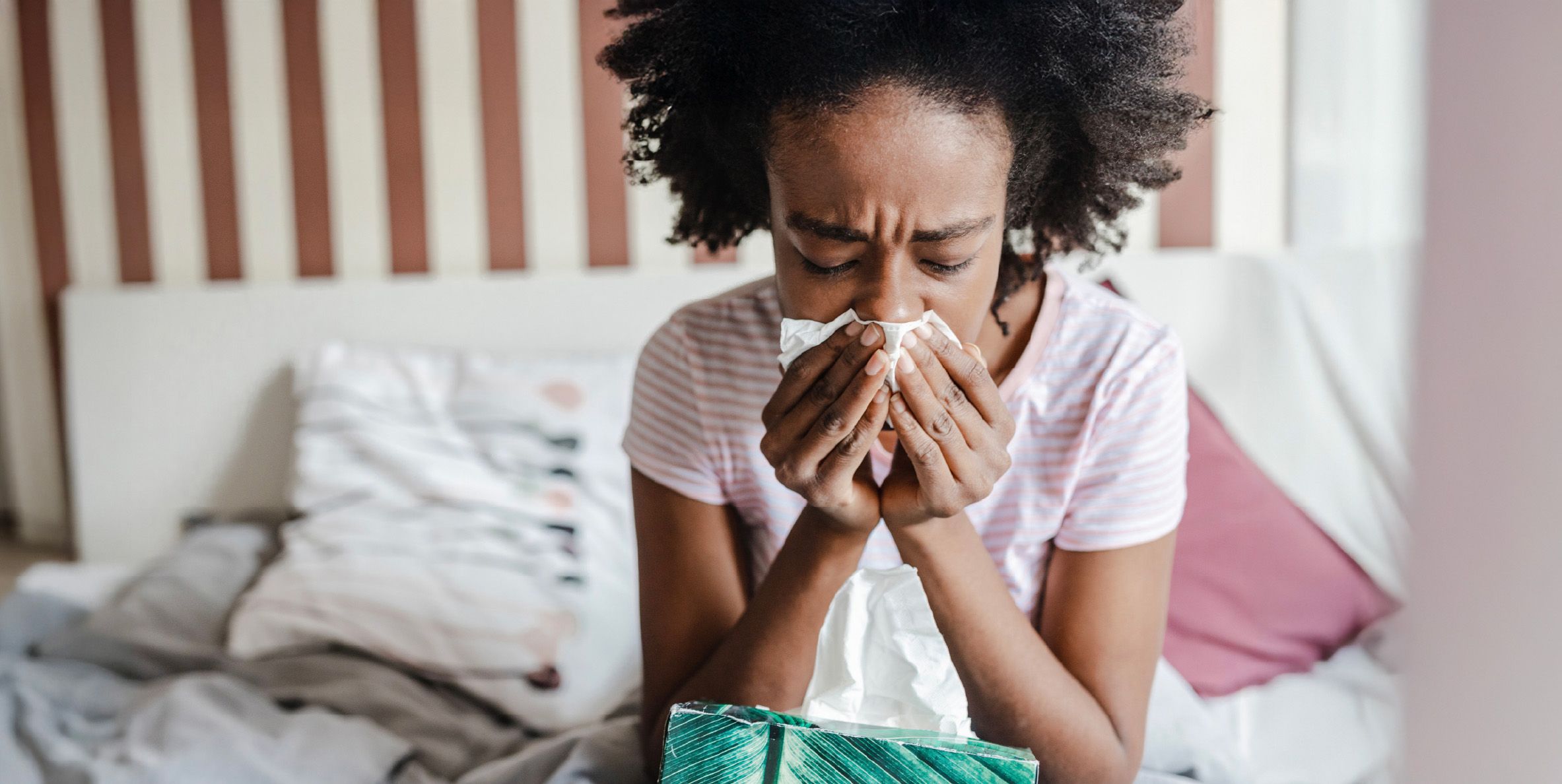 Girl sneezing into tissue on bed