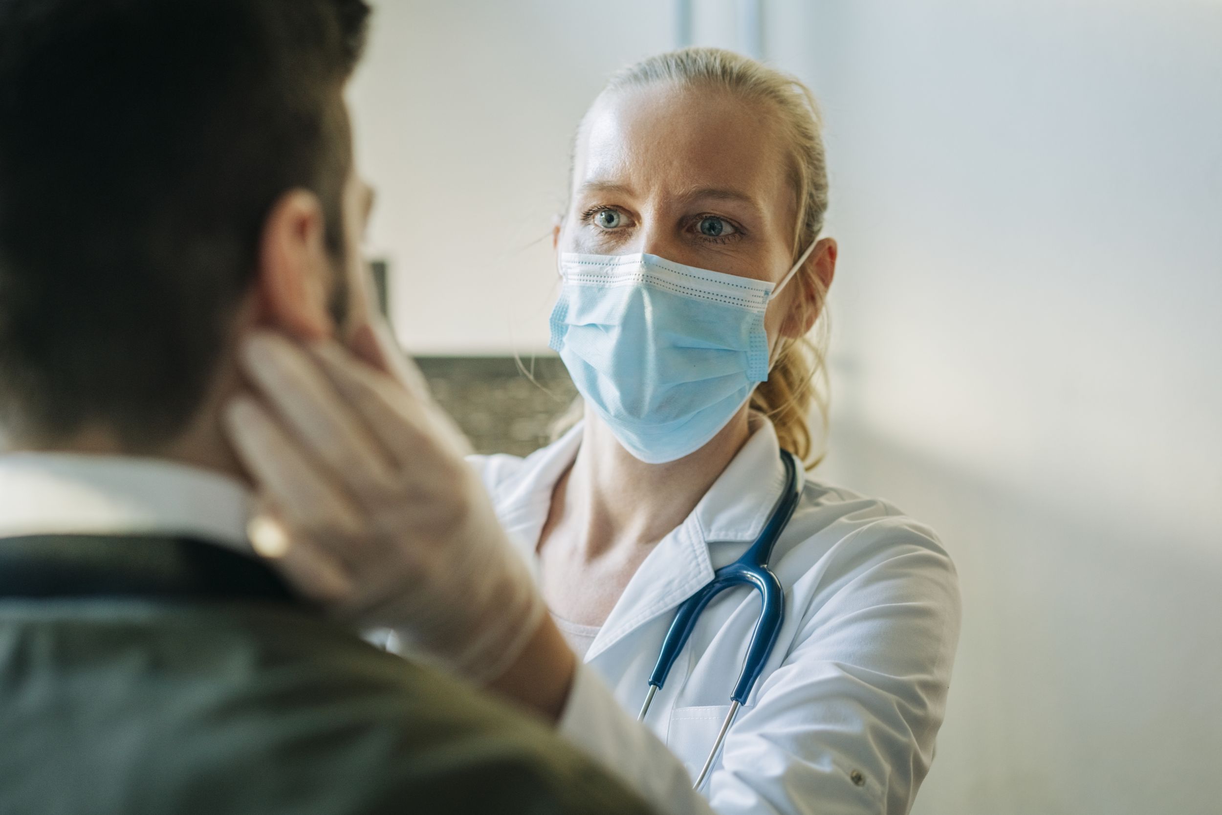 Female doctor wearing surgical mask examining infected patient. Mature healthcare worker checking mid adult man. They are at pharmacy.