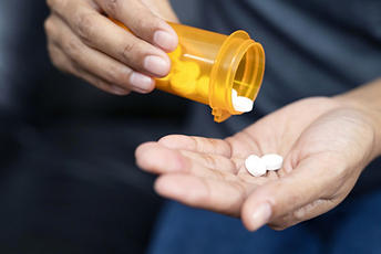 close up of someone holding an open pill bottle in one hand and tablets in the other hand