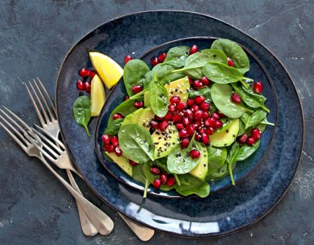  Salad with avocado, spinach, pomegranate, and sesame on a plate.