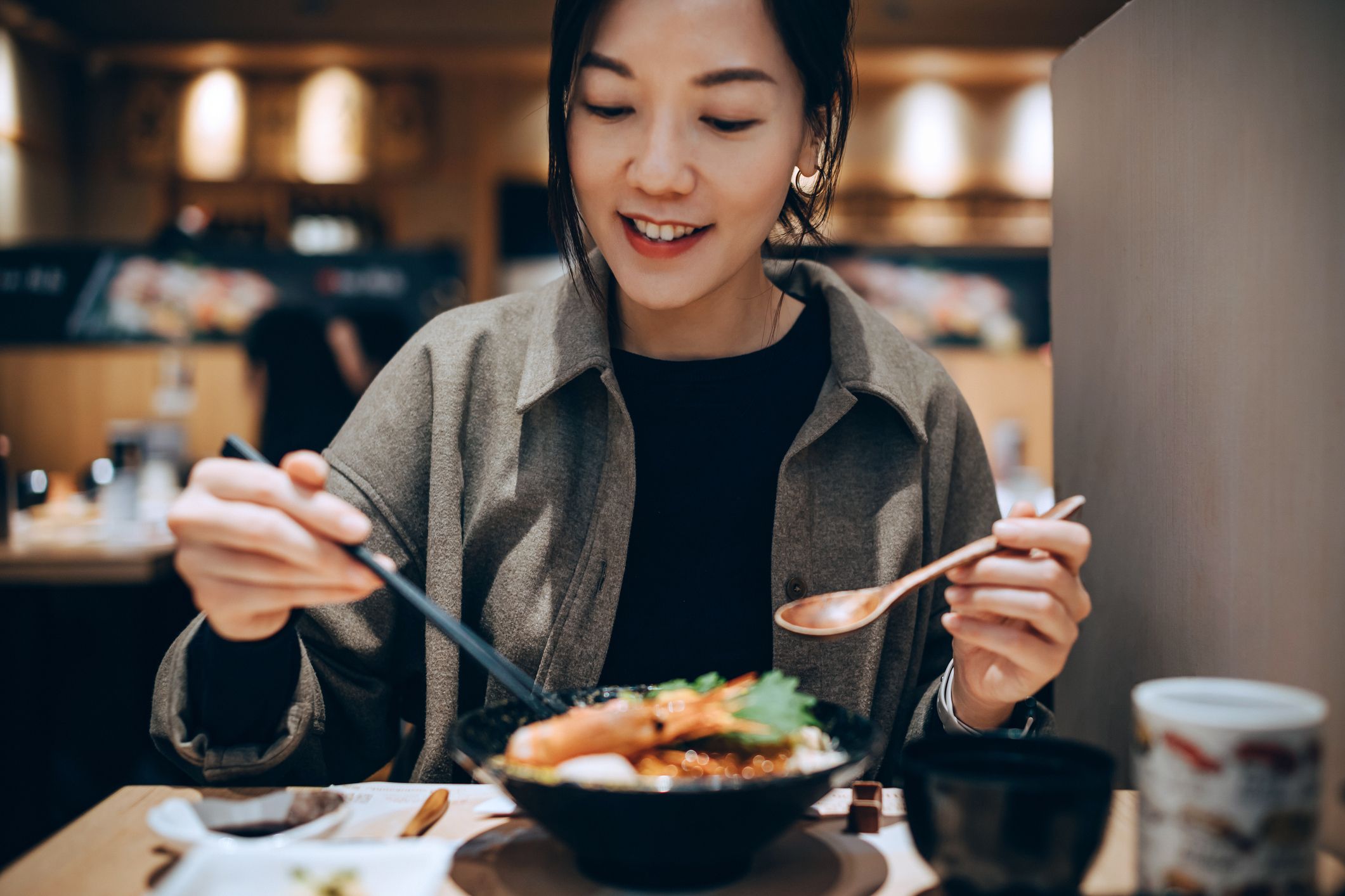 Beautiful smiling young woman enjoying delicate freshly served seafood sashimi rice bowl in Japanese restaurant. Authentic Japanese cuisine and food culture. People and food concept