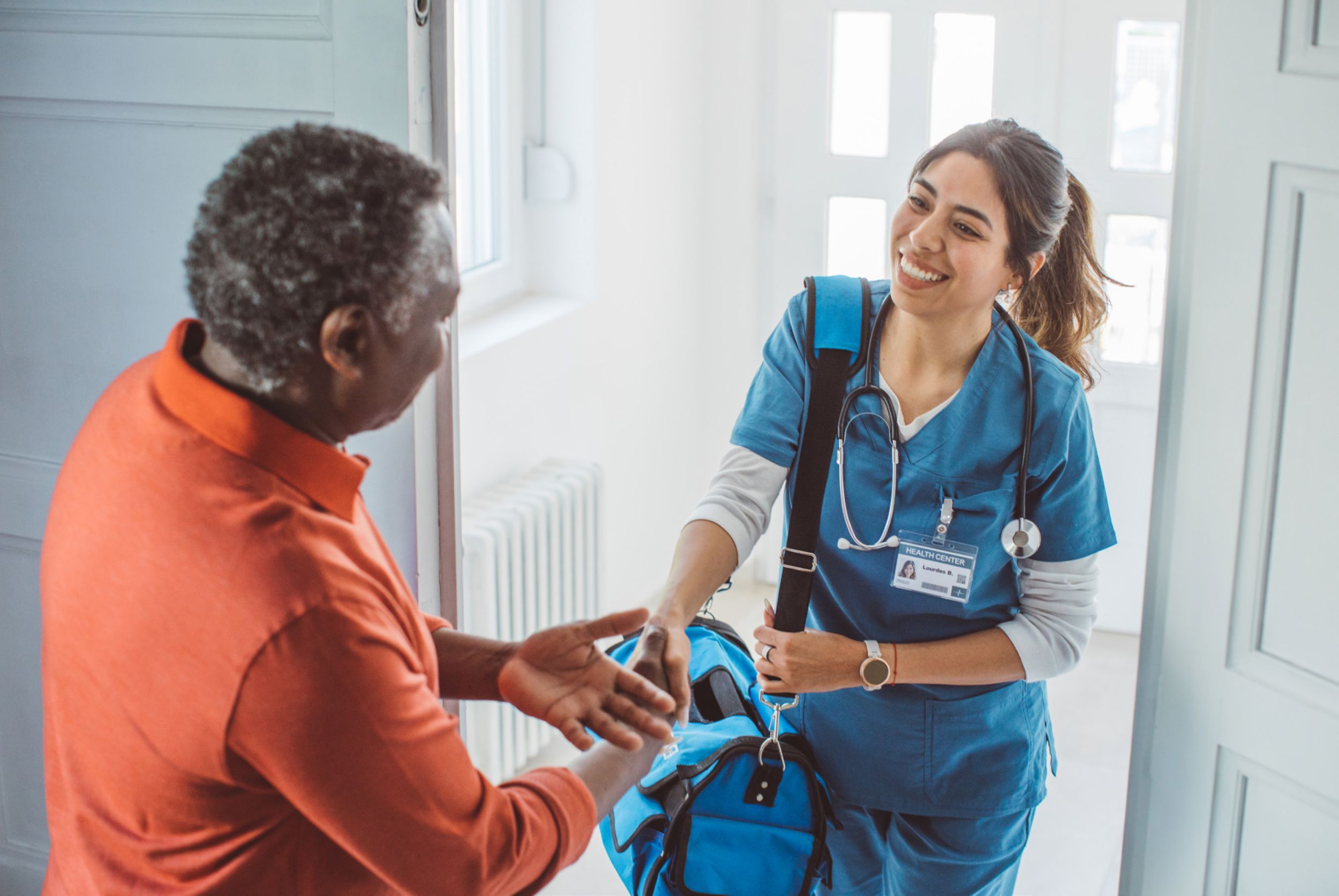 Mobile phlebotomist visiting mature patient at home. She is holding bag and entering at patient's home.