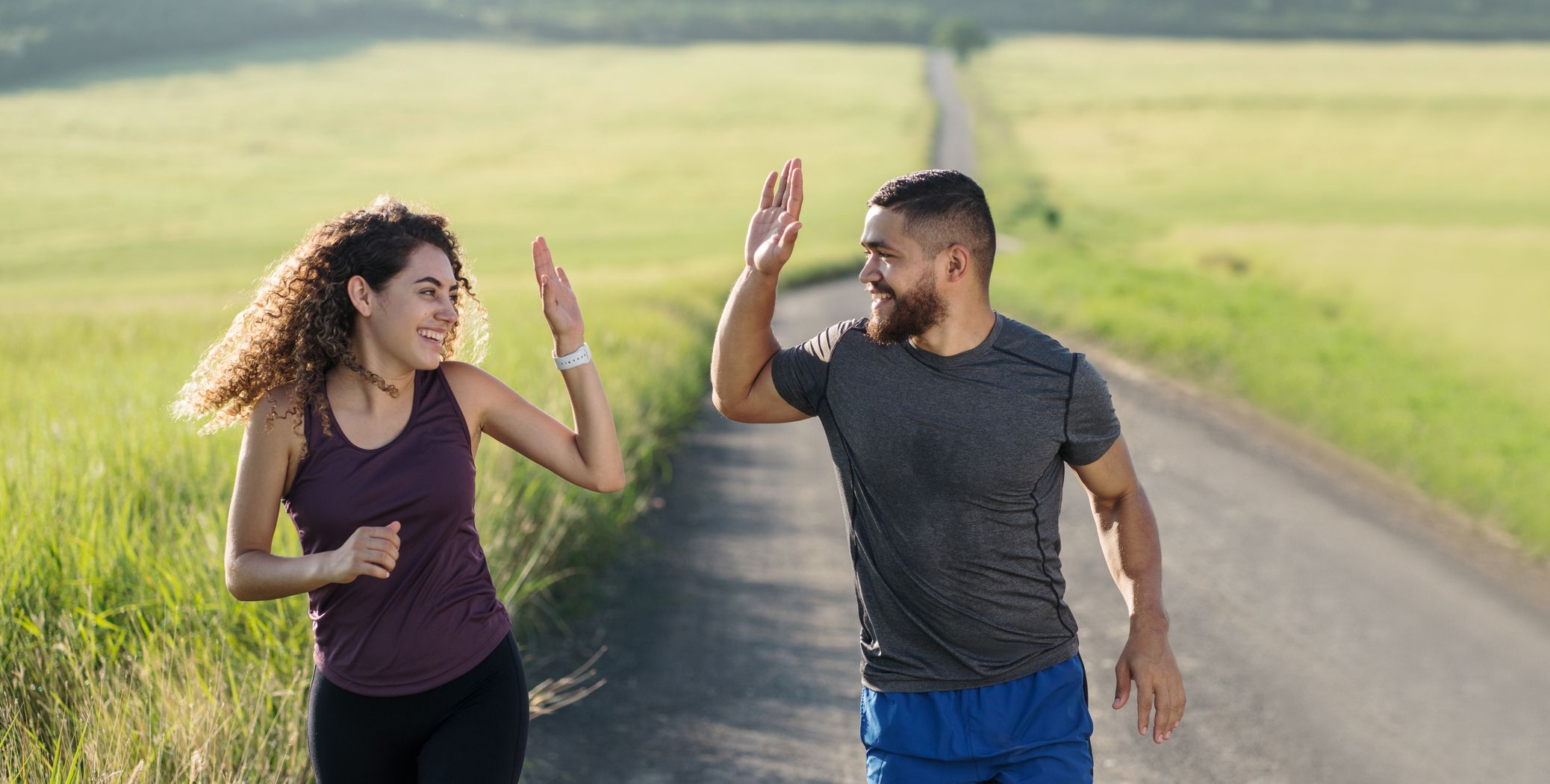A fun young latin couple running in the countryside, high-fiving and smiling at each other.