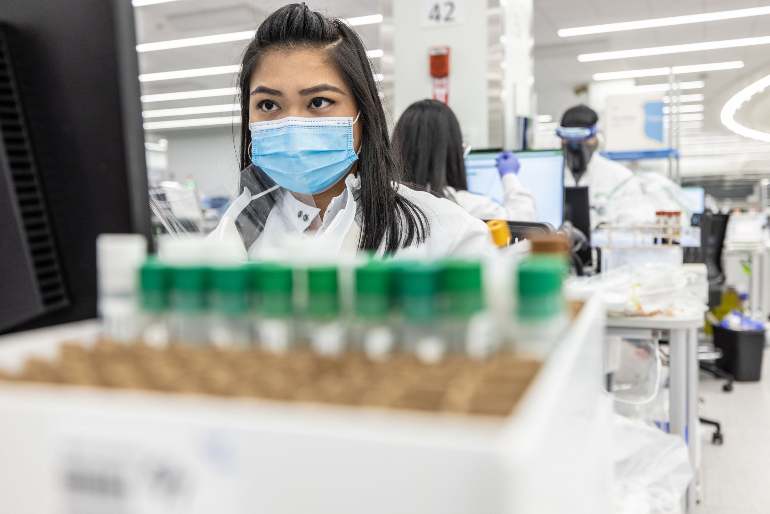 Female lab technician at a computer with other lab techs working in the background