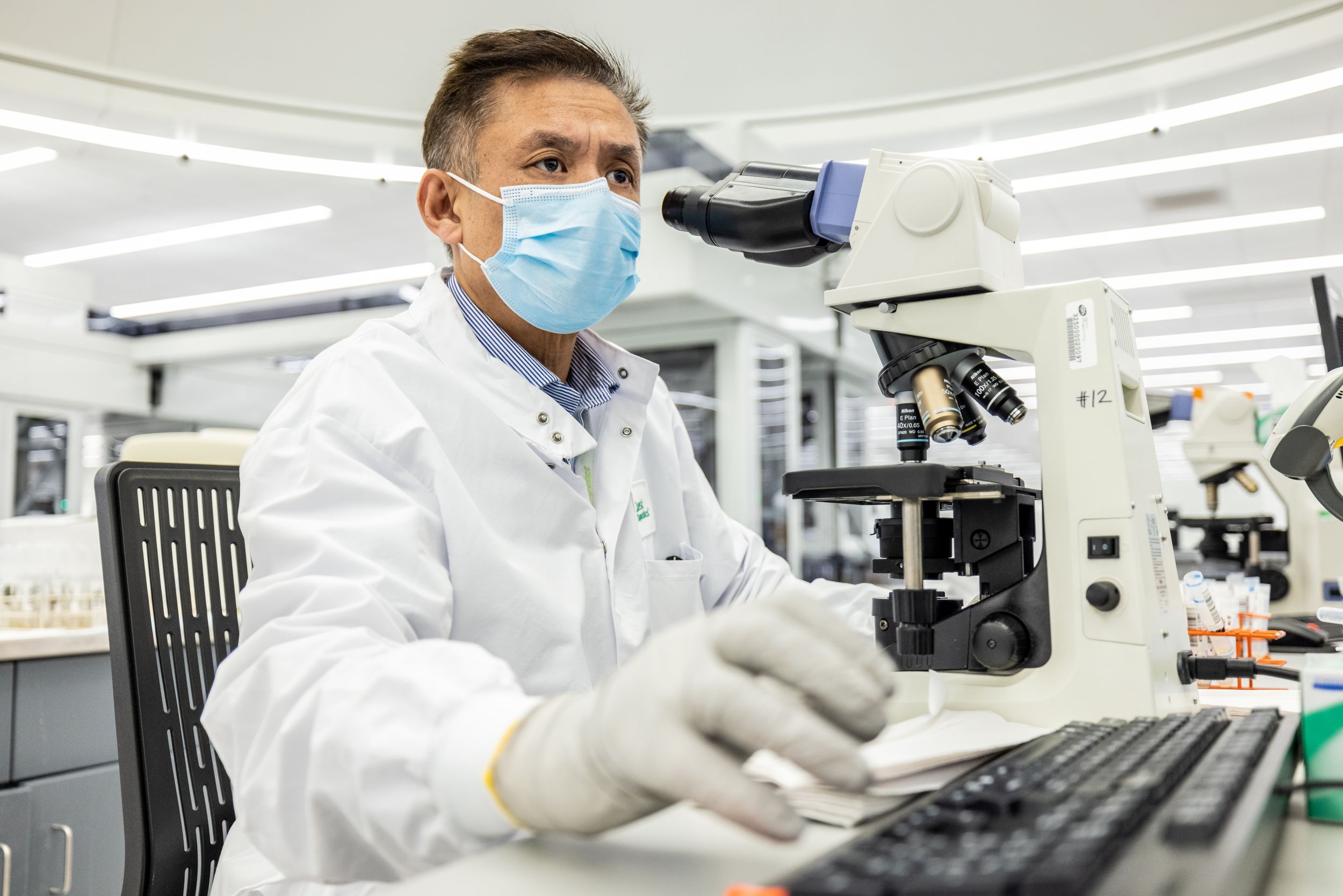 physician wearing white lab coat, analyzing medical sample in a microscope