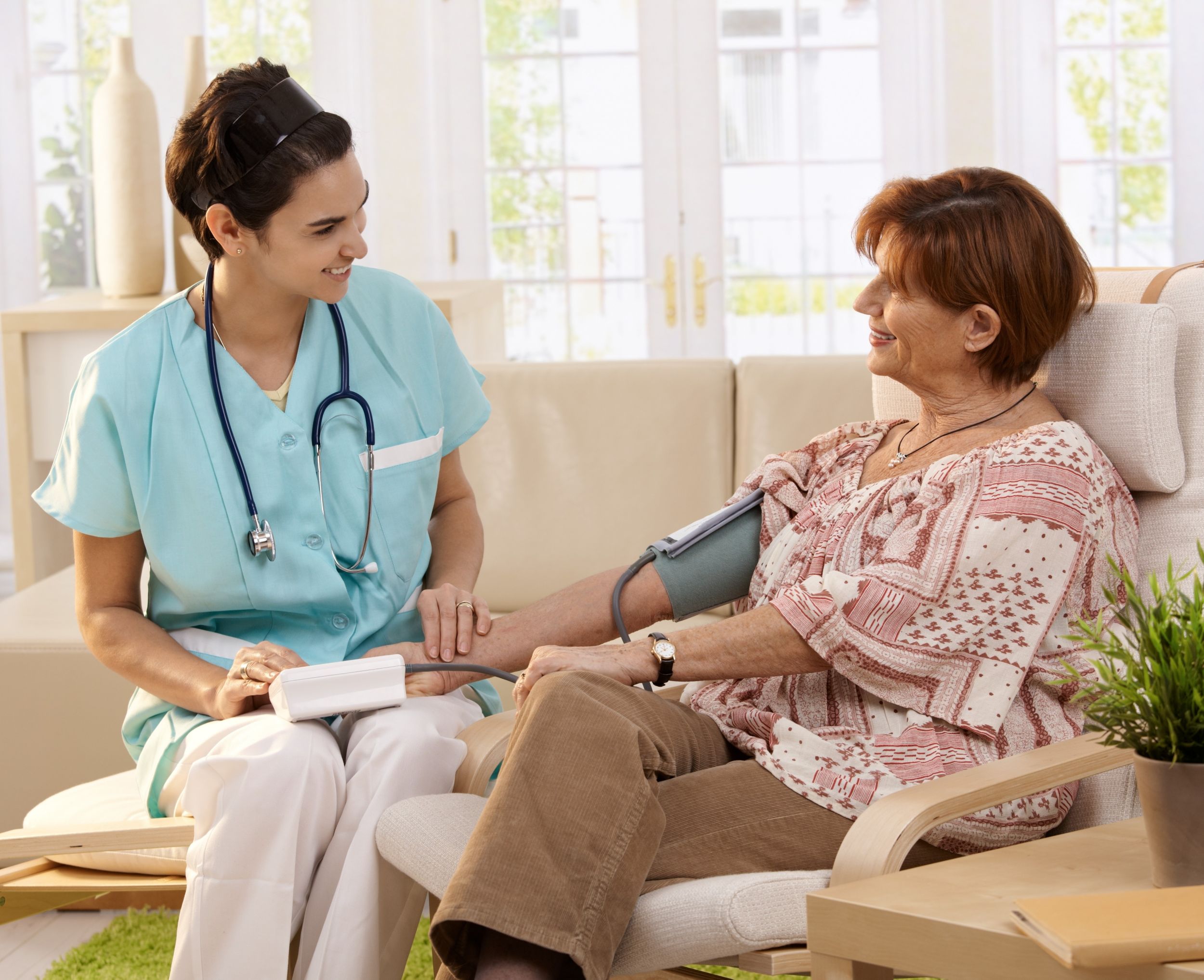 Female nurse measuring blood pressure of woman at home