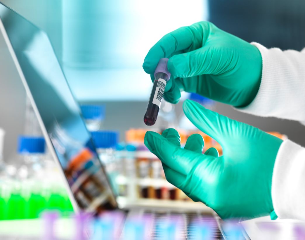 lab tech with test tube in front of laptop