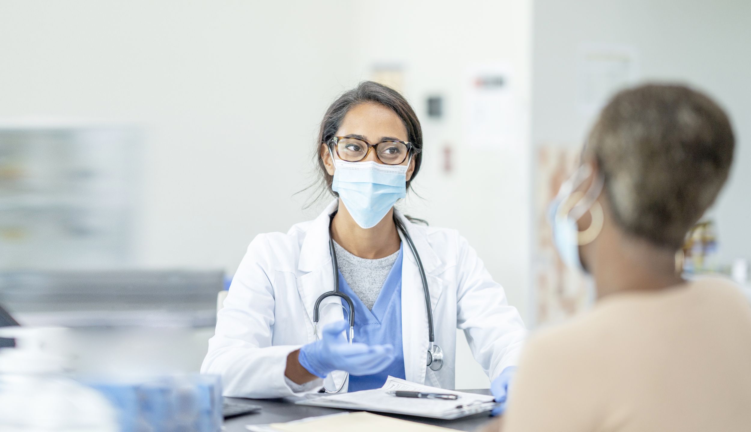 Female doctor and patient in personal protective equipment at medical exam.