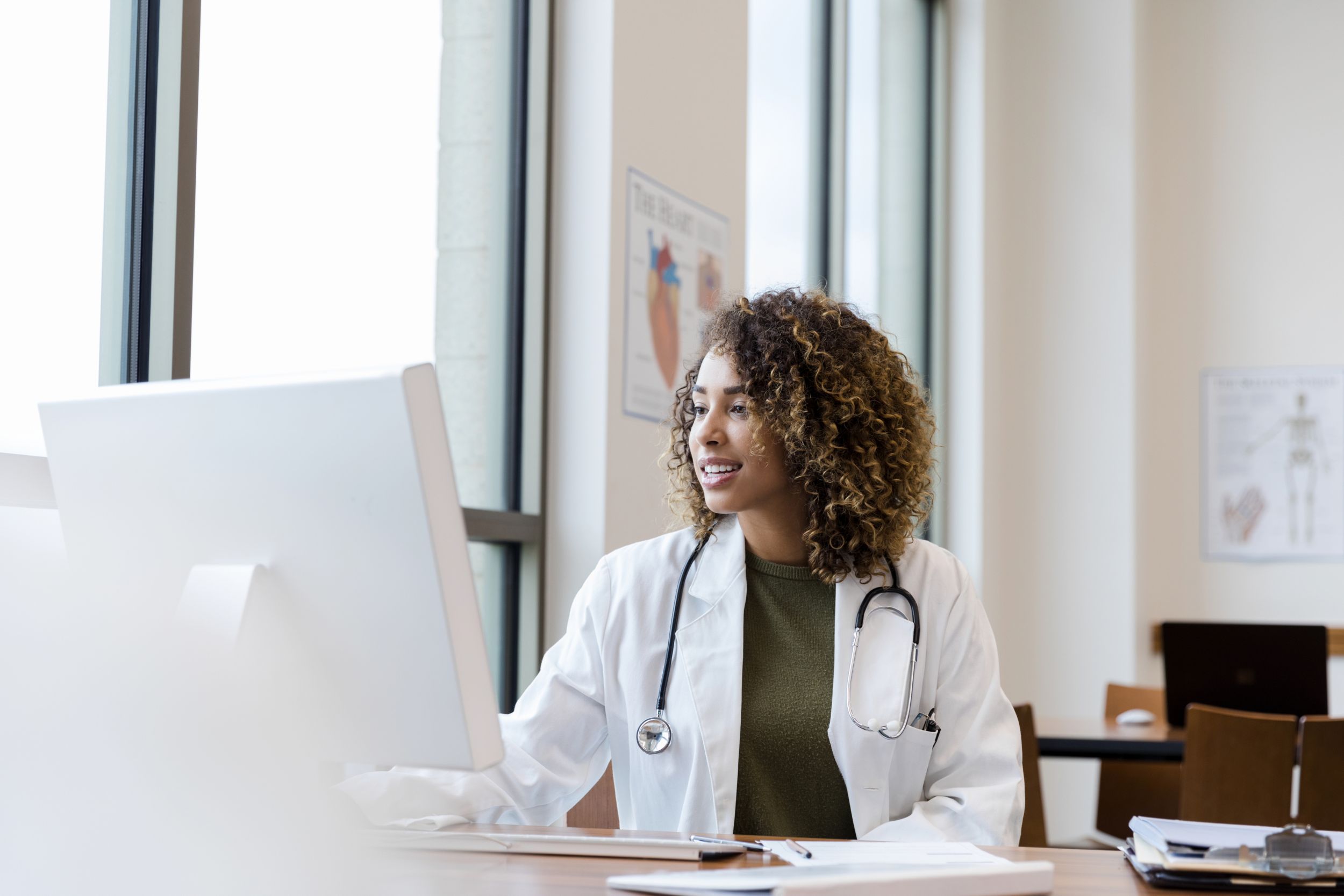 An adult female doctor reviews her patient's records on her computer in her office.