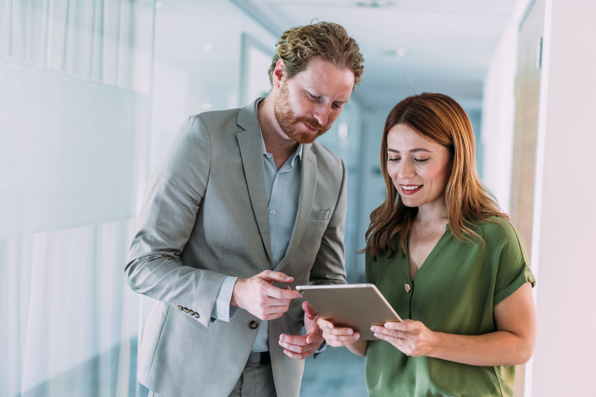 Shot of a two confident business persons talking in the work place. Two colleagues using a digital tablet while walking in a modern office. Businessman and businesswoman in meeting discussing business strategy. Business coworkers working together in the office.
